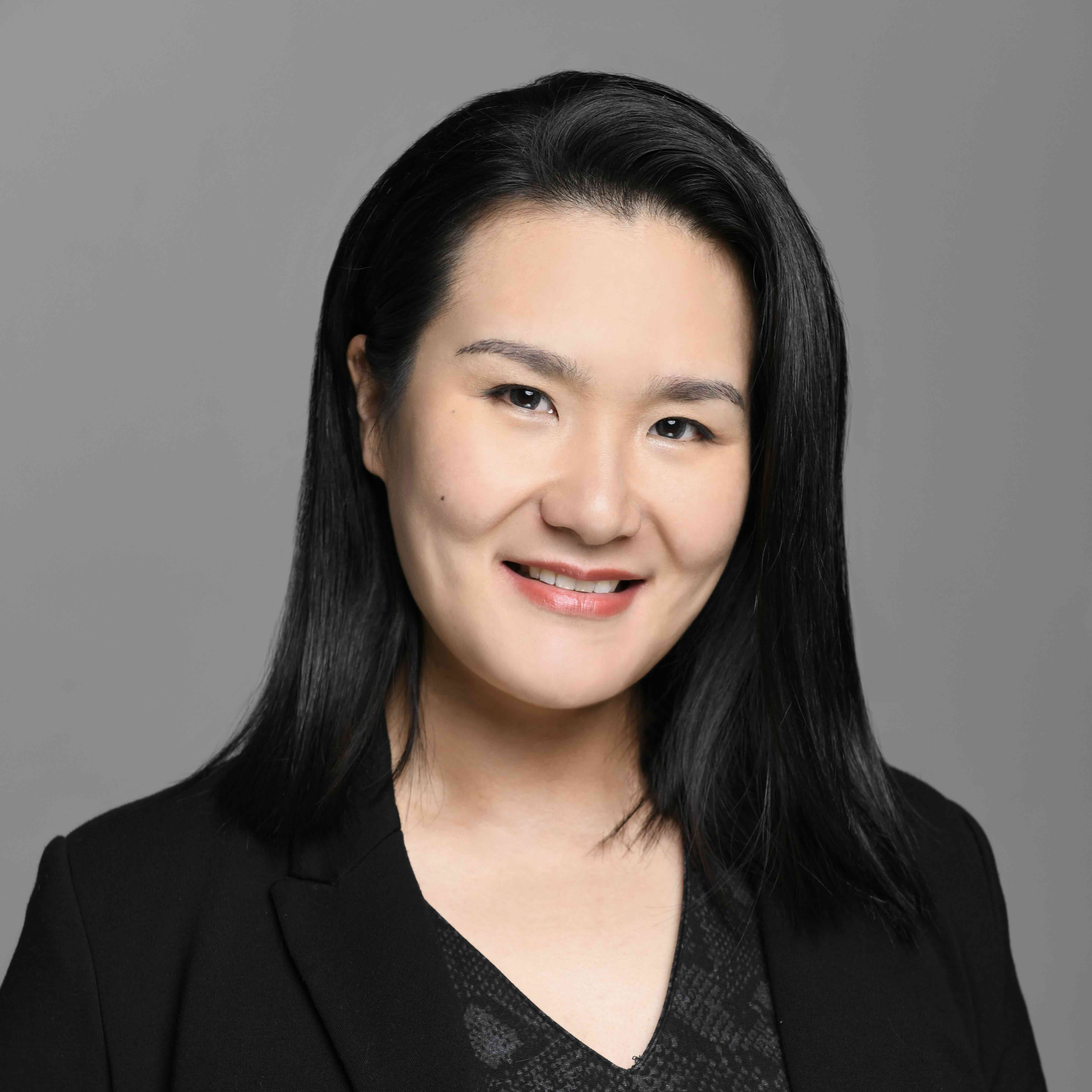 Headshot of a smiling woman in a black blazer against a gray background.