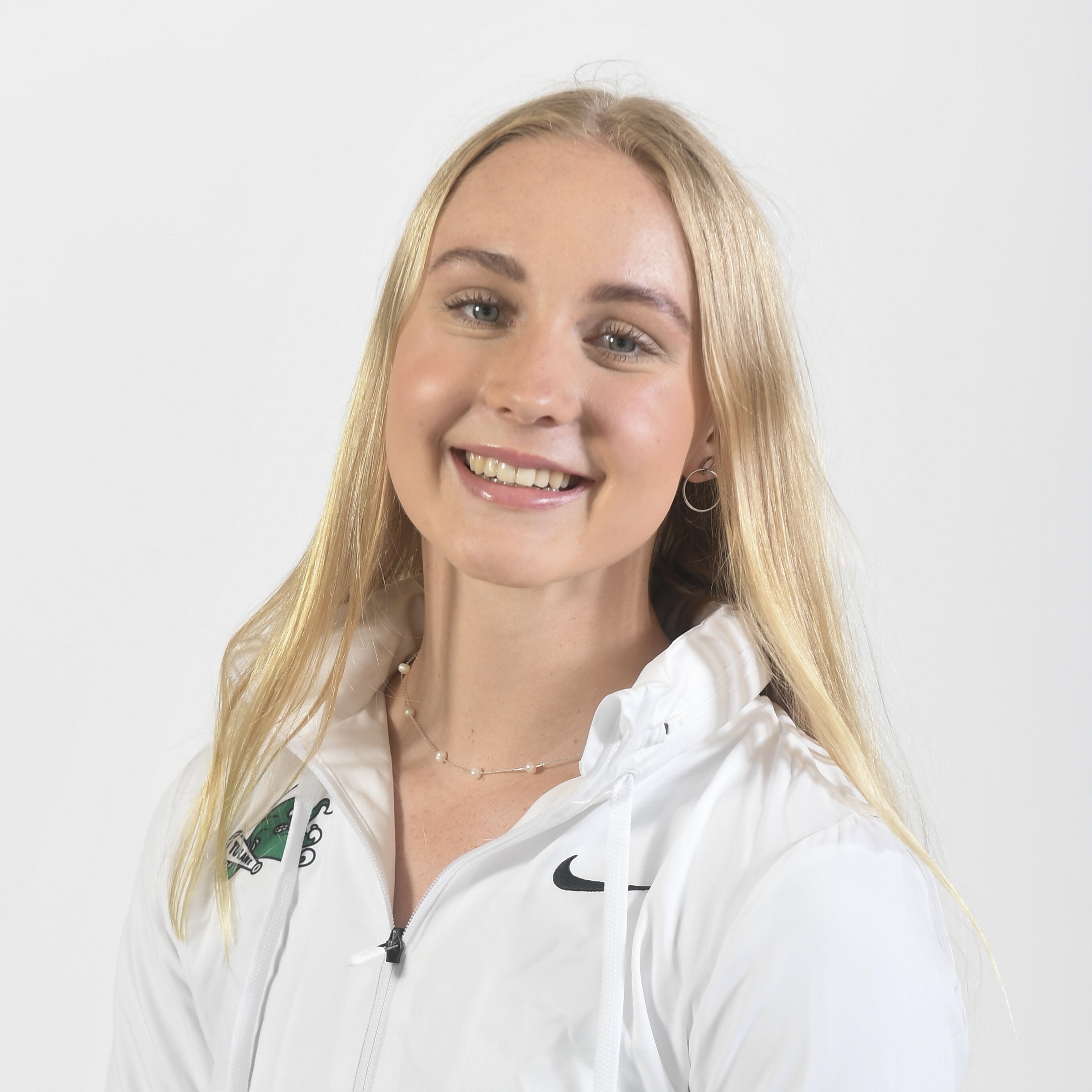 Blonde woman in white Nike jacket smiles at camera.