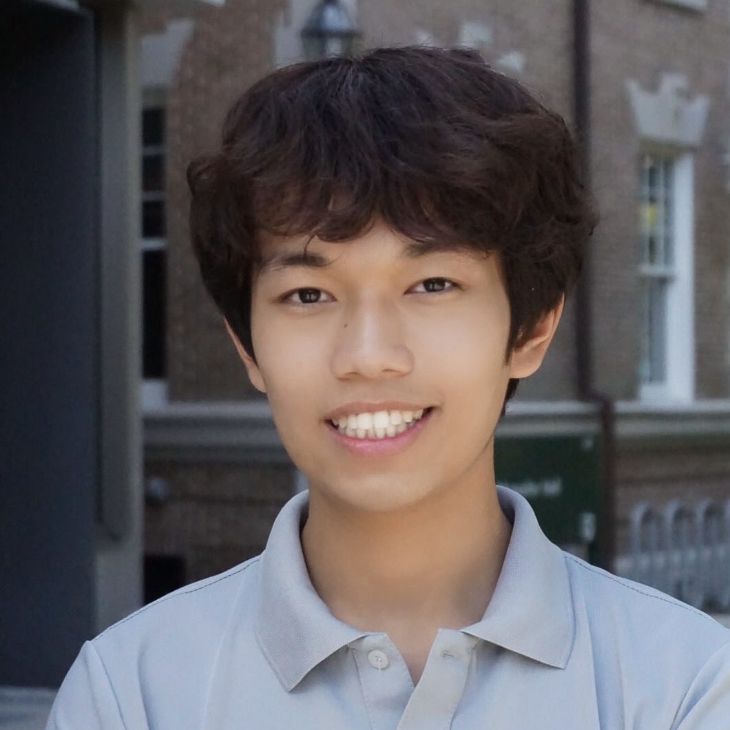 Portrait of a young man smiling, outdoor setting with brick building in background.