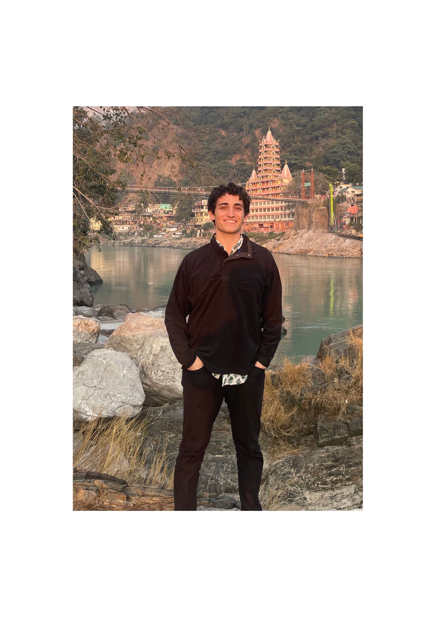 man smiling next to river with temple in background