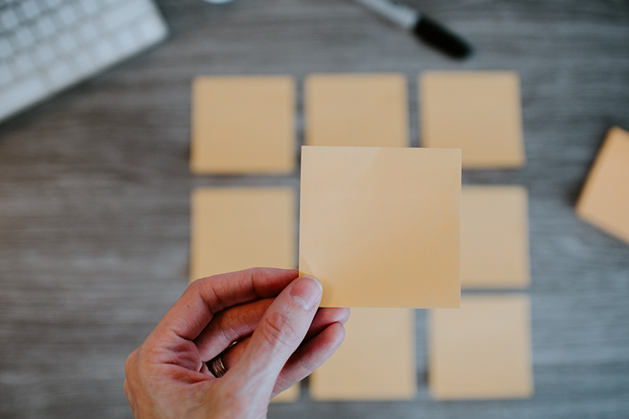 Person holding a blank sticky note with a grid of sticky notes on a table.