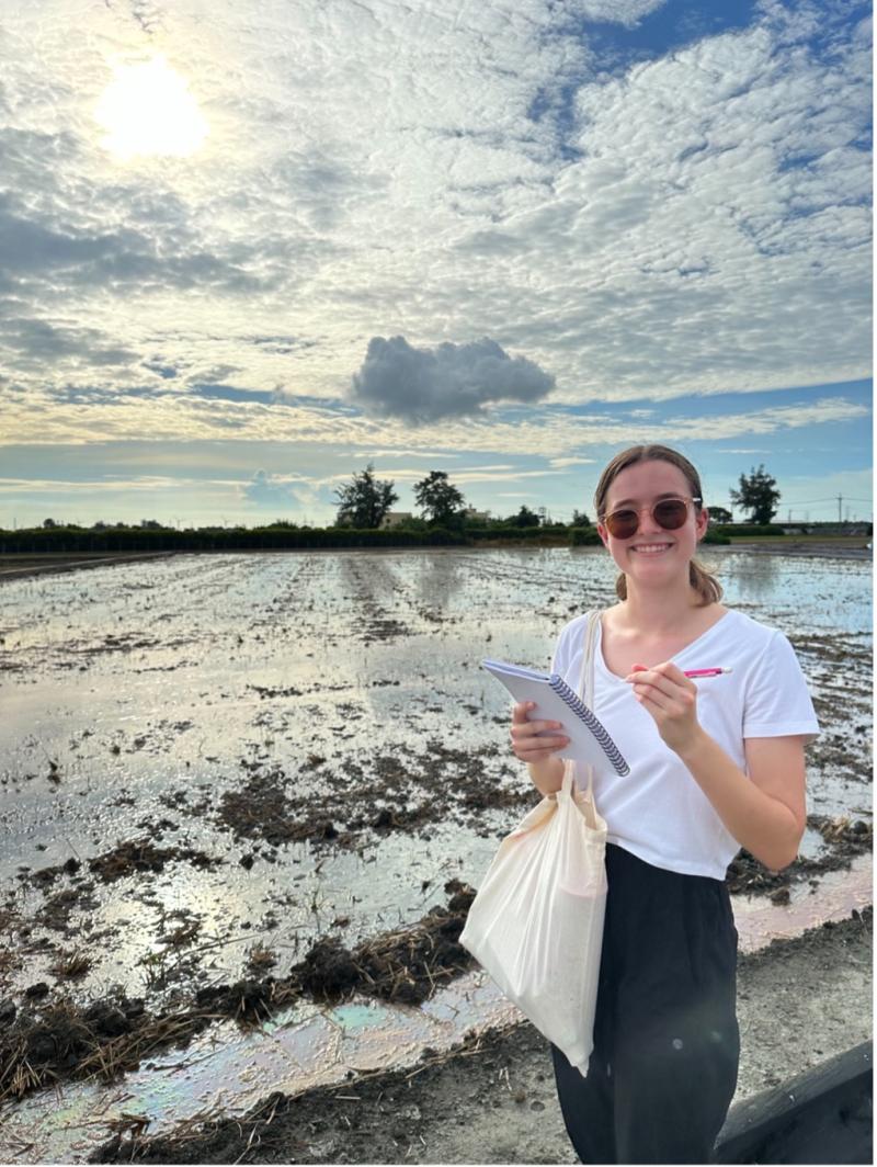 woman smiling with notebook in front of wet field